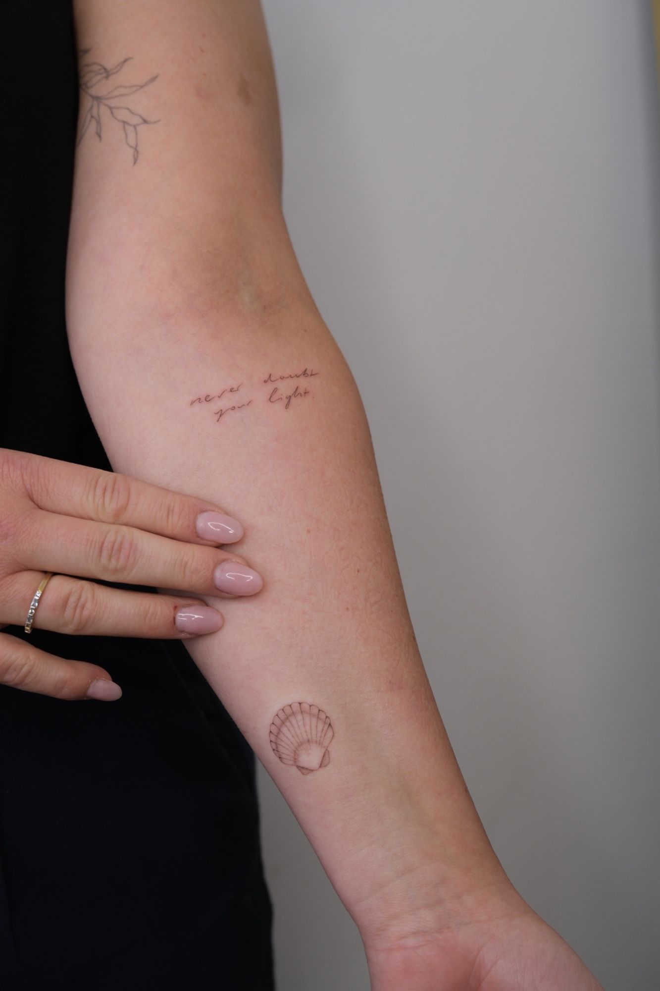 Schrift und Muschel im Fineline Style auf Oberarm von @alinaatattoo in 20457