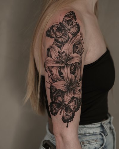 Lilien & Schmetterlinge im Black Gray Style auf Oberarm von Inc. Tattoo Studio in 39108