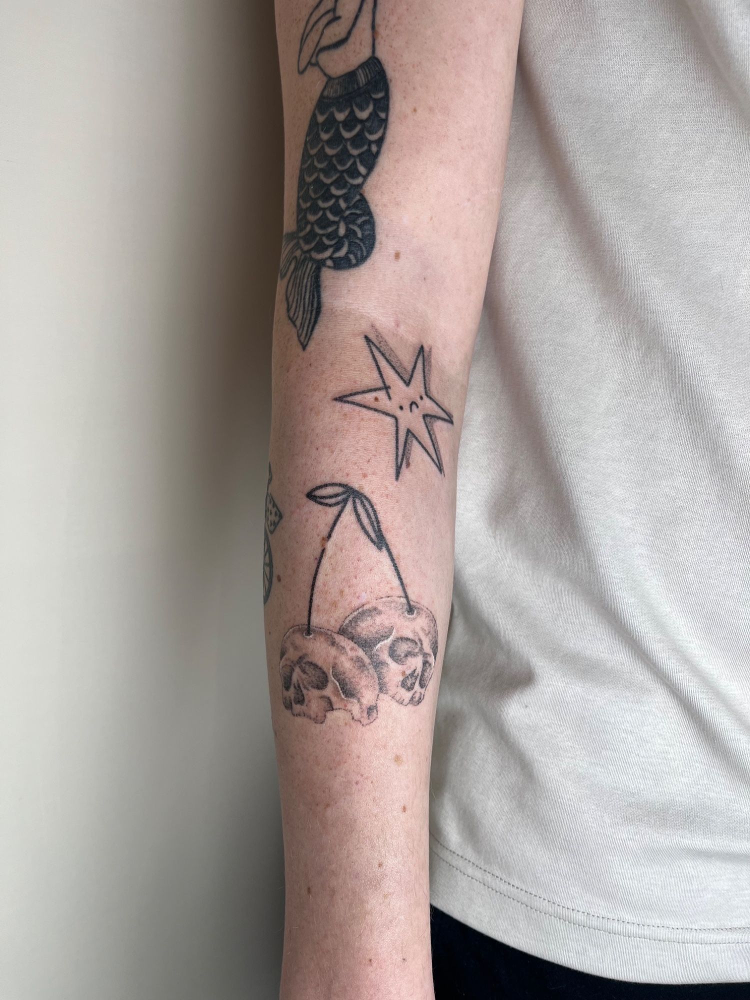 Realistische Kirschen Totenköpfe und trauriger Stern im Black & Gray Style auf Unterarm von nur so tattoos