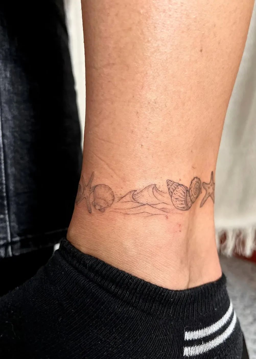 Maritime anklet with starfish, shells, and waves as a fineline tattoo on the ankle