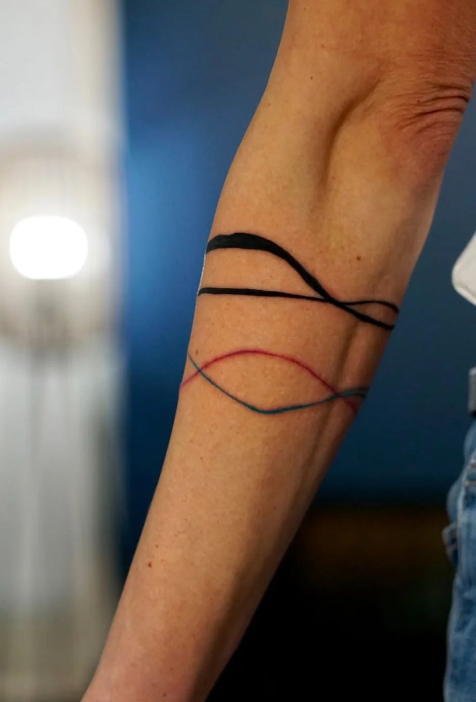 Armring tattoo with black, red, and blue lines on the forearm