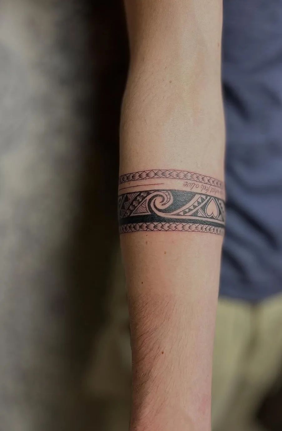 Tribal style armring tattoo with waves and hearts on forearm