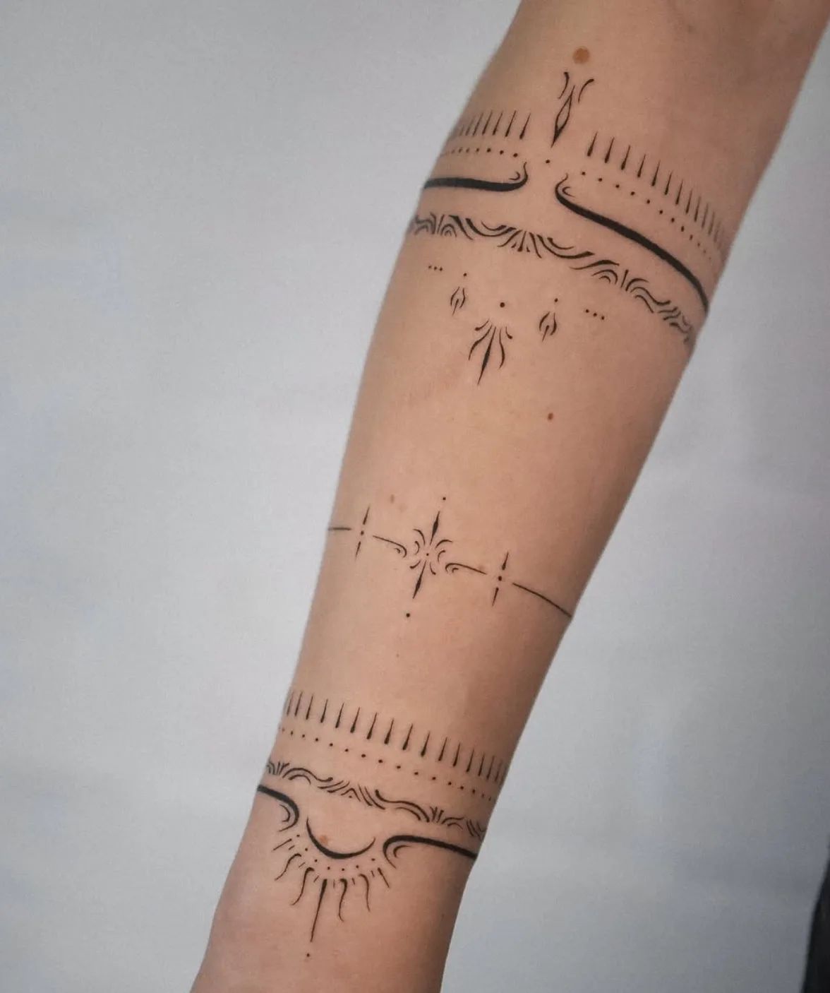 Delicate fine line armring tattoo with geometric patterns and sun design on the forearm