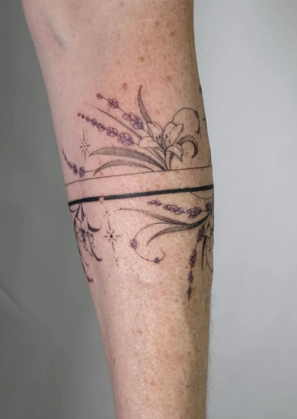 Armring tattoo with lavender and lilies in fine line on forearm