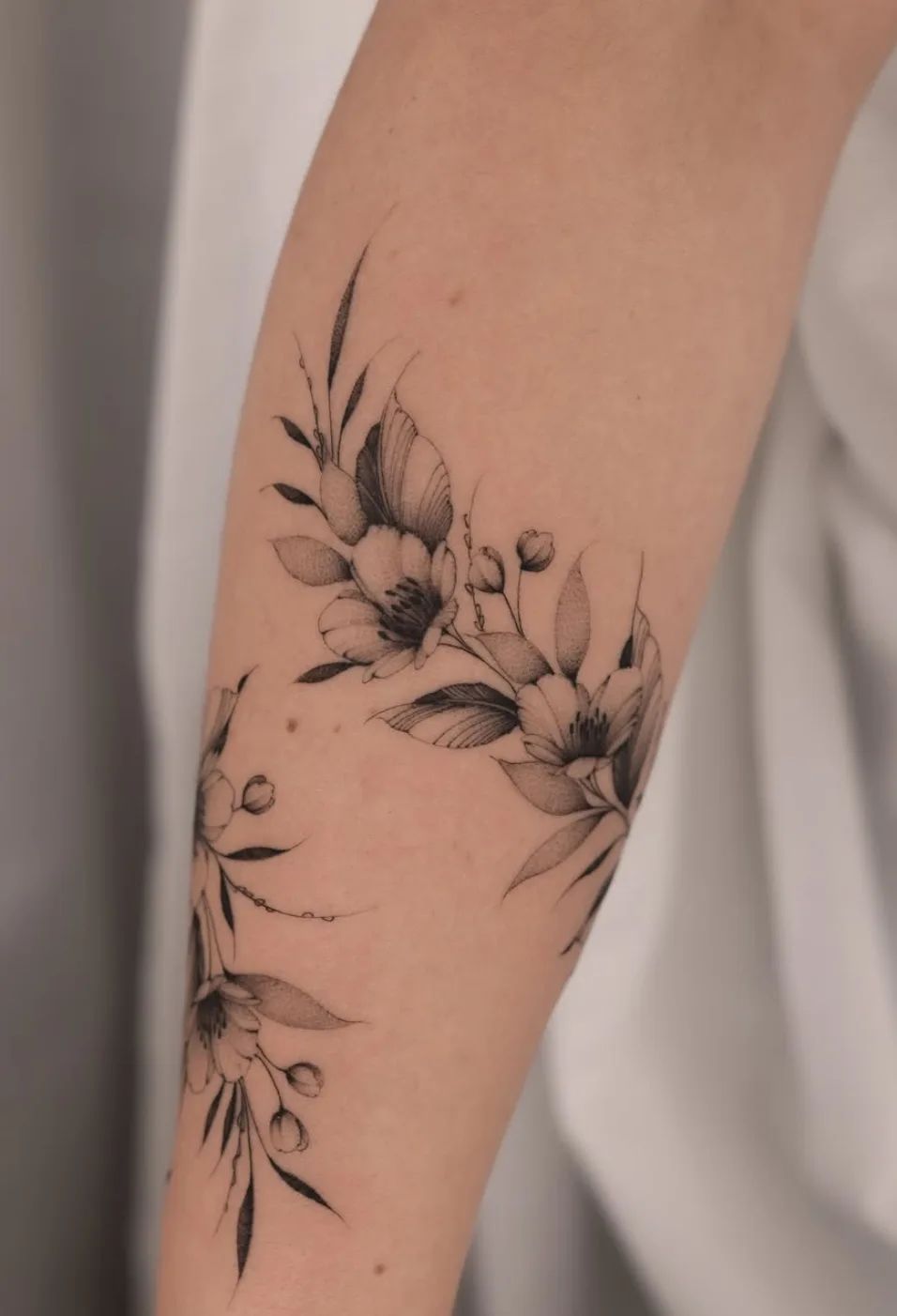 Armring tattoo with flowers and leaves in fine line style on forearm