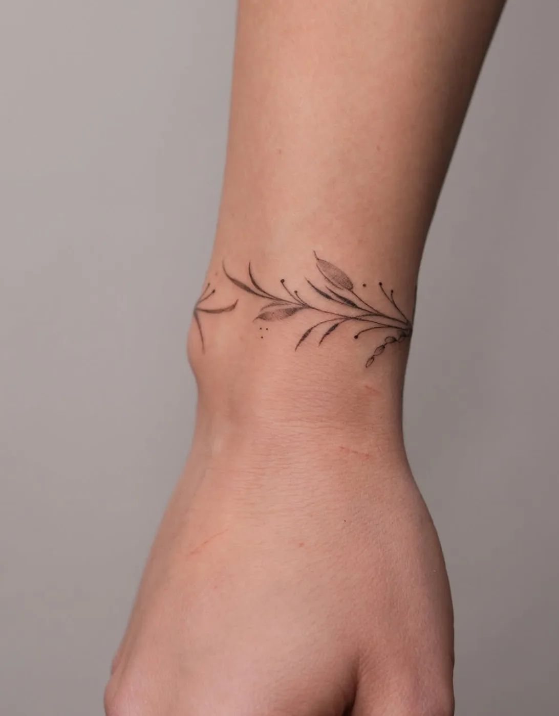 Fine line armring tattoo with delicate leaves and dots on the wrist