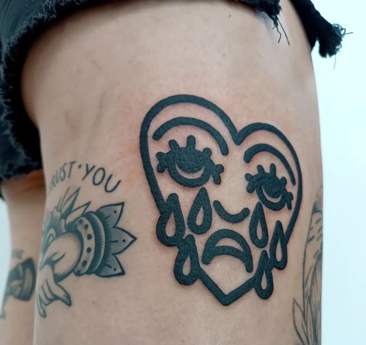 Cartoon style heart tattoo with crying face on thigh