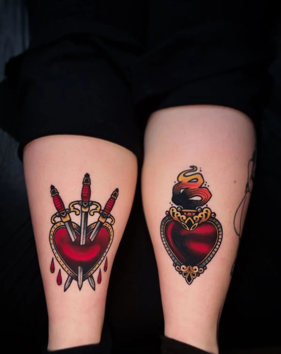 Two traditional heart tattoos, one with three daggers and blood drops, the other with flames, on the thighs
