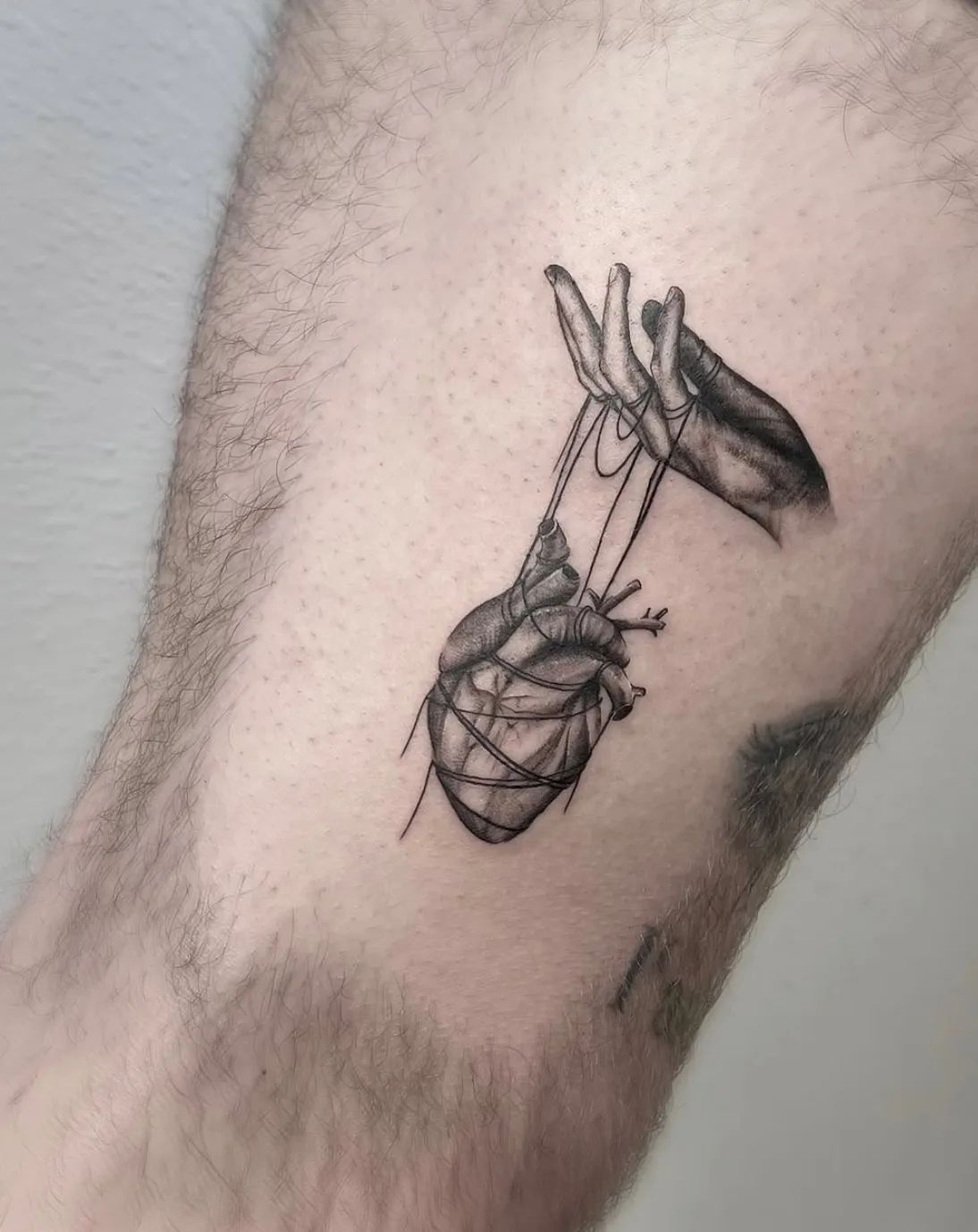 Realistic heart tattoo with hands and strings in fine line style on upper arm