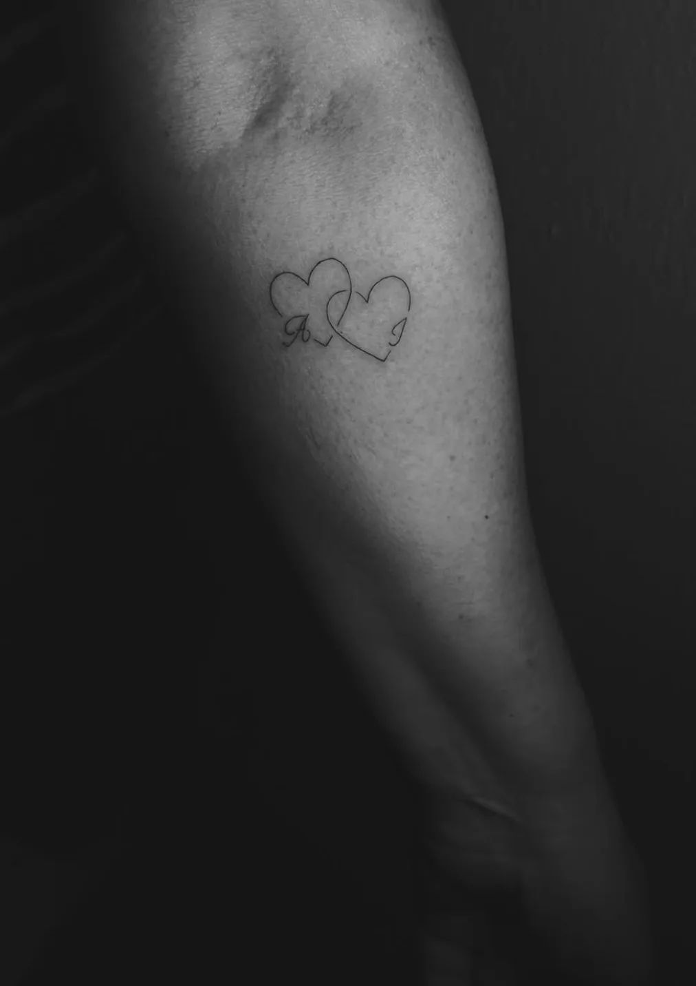 Two intertwined hearts fine line tattoo with initials A and J on upper arm