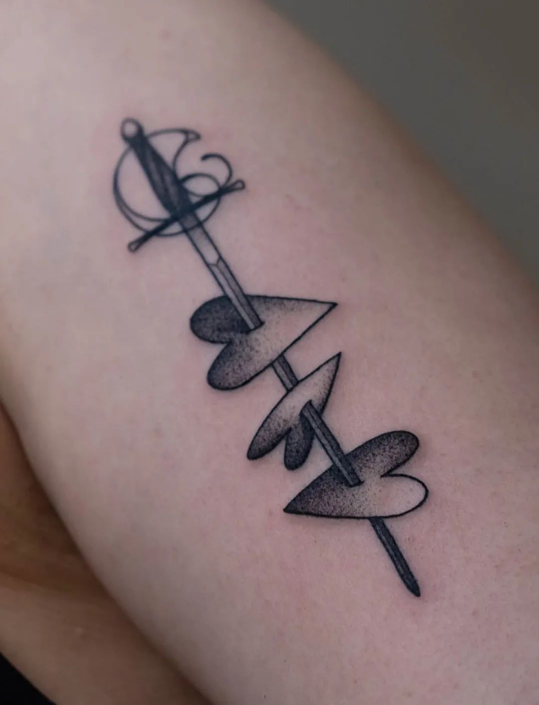 Sword tattoo with pierced hearts in dotwork style on upper arm