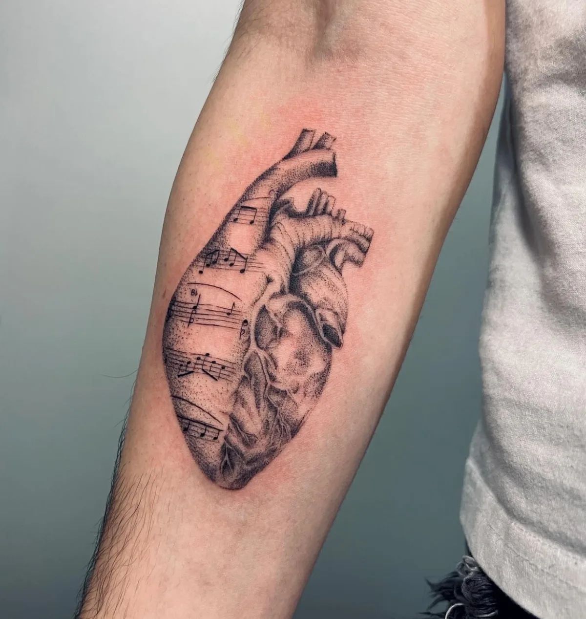 Realistic heart tattoo with musical notes in dotwork style on forearm