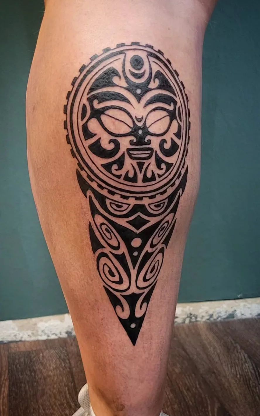 Maori tattoo with Tiki face and tribal patterns on leg