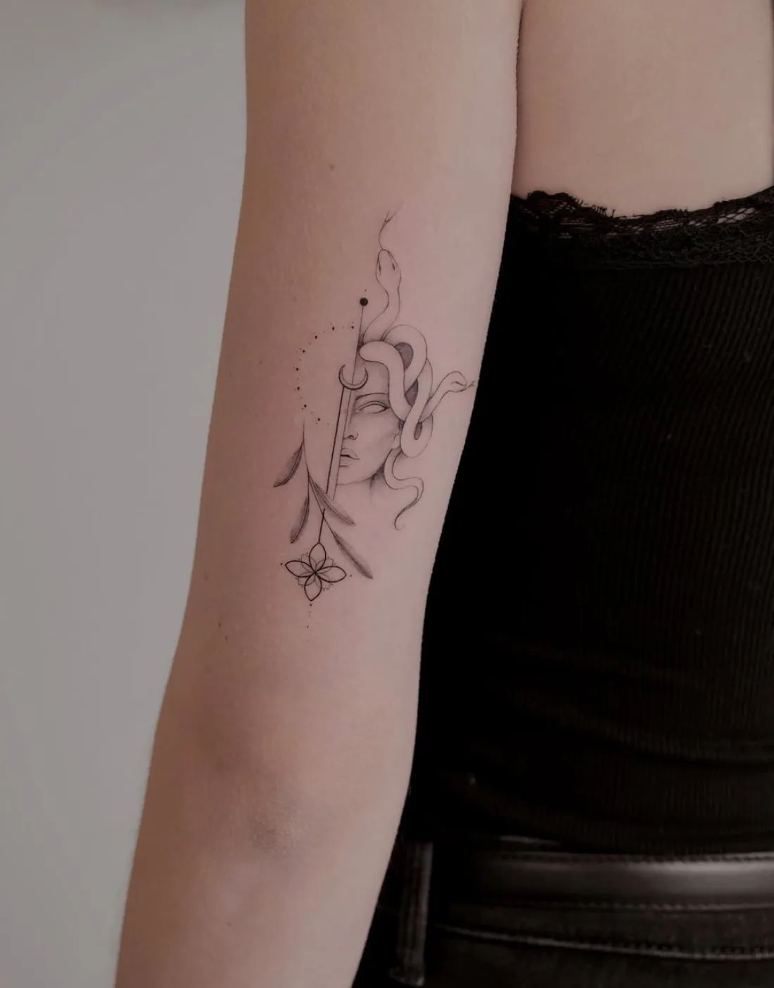 Medusa Tattoo Fineline mit Schwert, Blättern und Blume am Oberarm