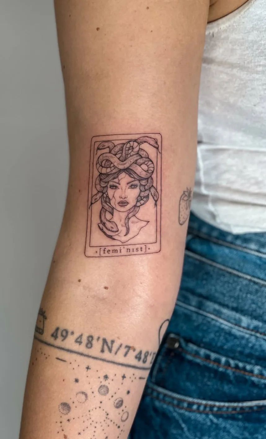 Medusa Tattoo im Fineline-Stil als Tarotkarte mit „feminist“ Schriftzug am Oberarm