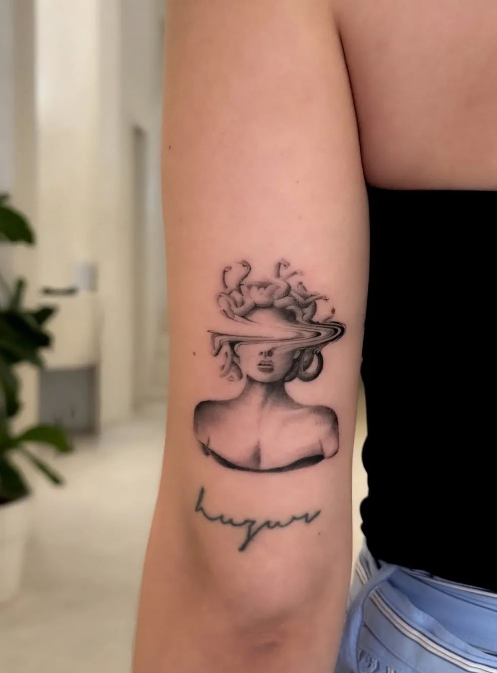 Medusa Tattoo im surrealistischen Stil am Oberarm mit Schriftzug