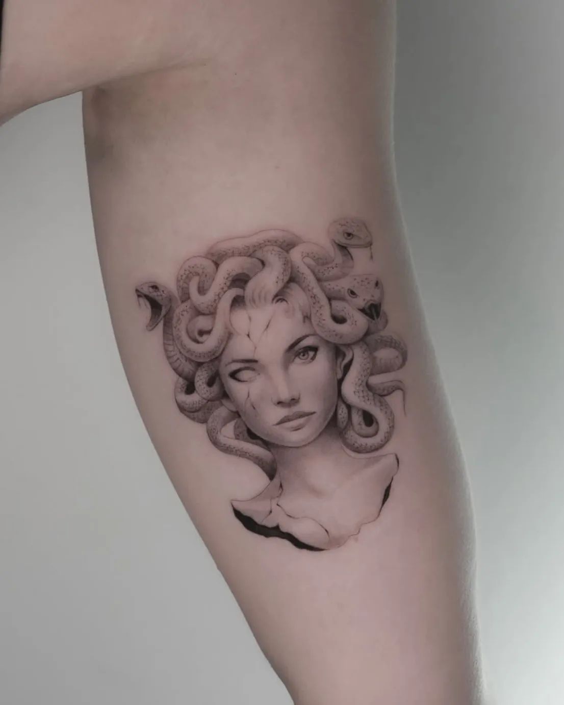 Medusa Tattoo im Fineline-Stil als zerbrochene Büste am Oberarm