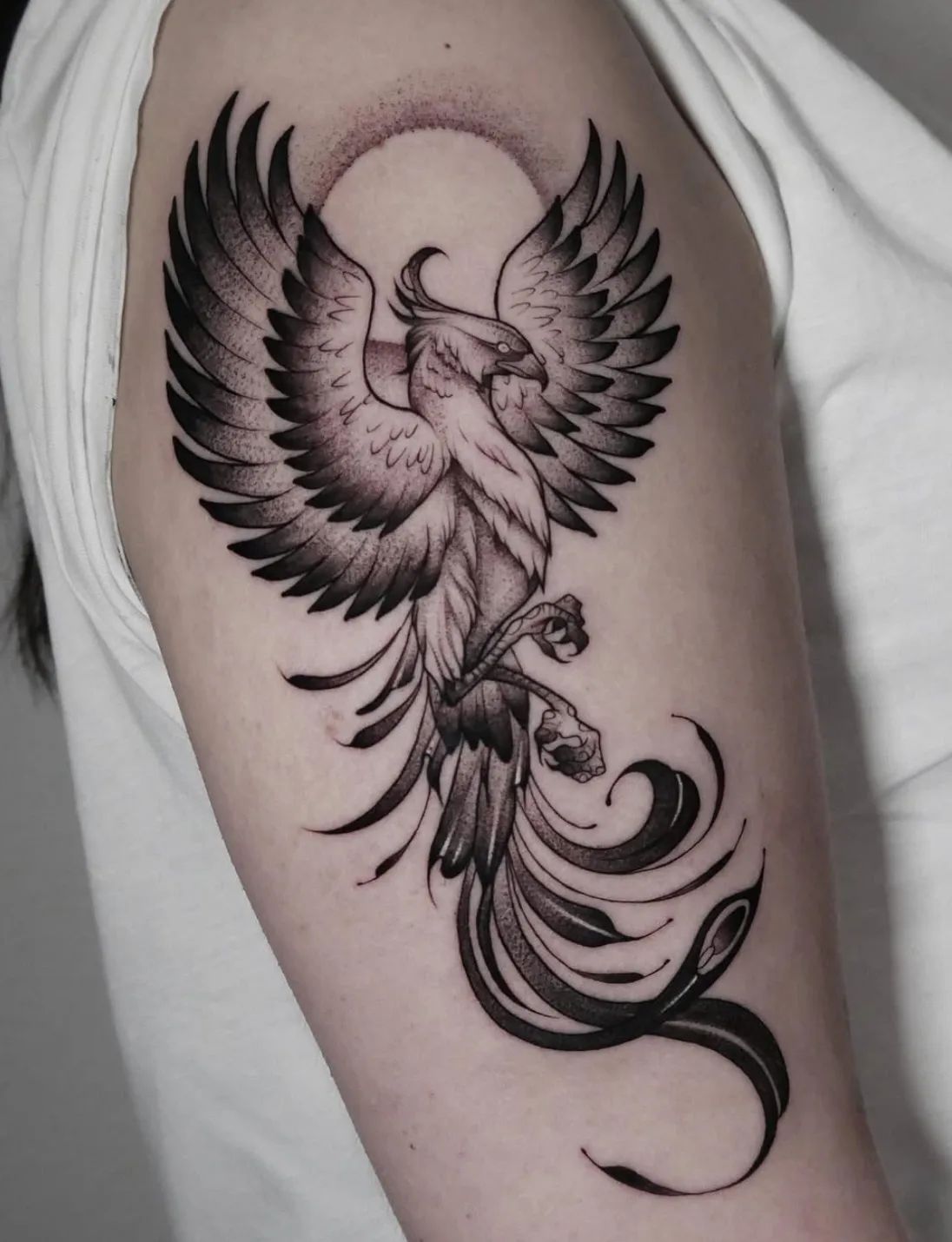 Blackwork phoenix tattoo with dot pattern halo on upper arm