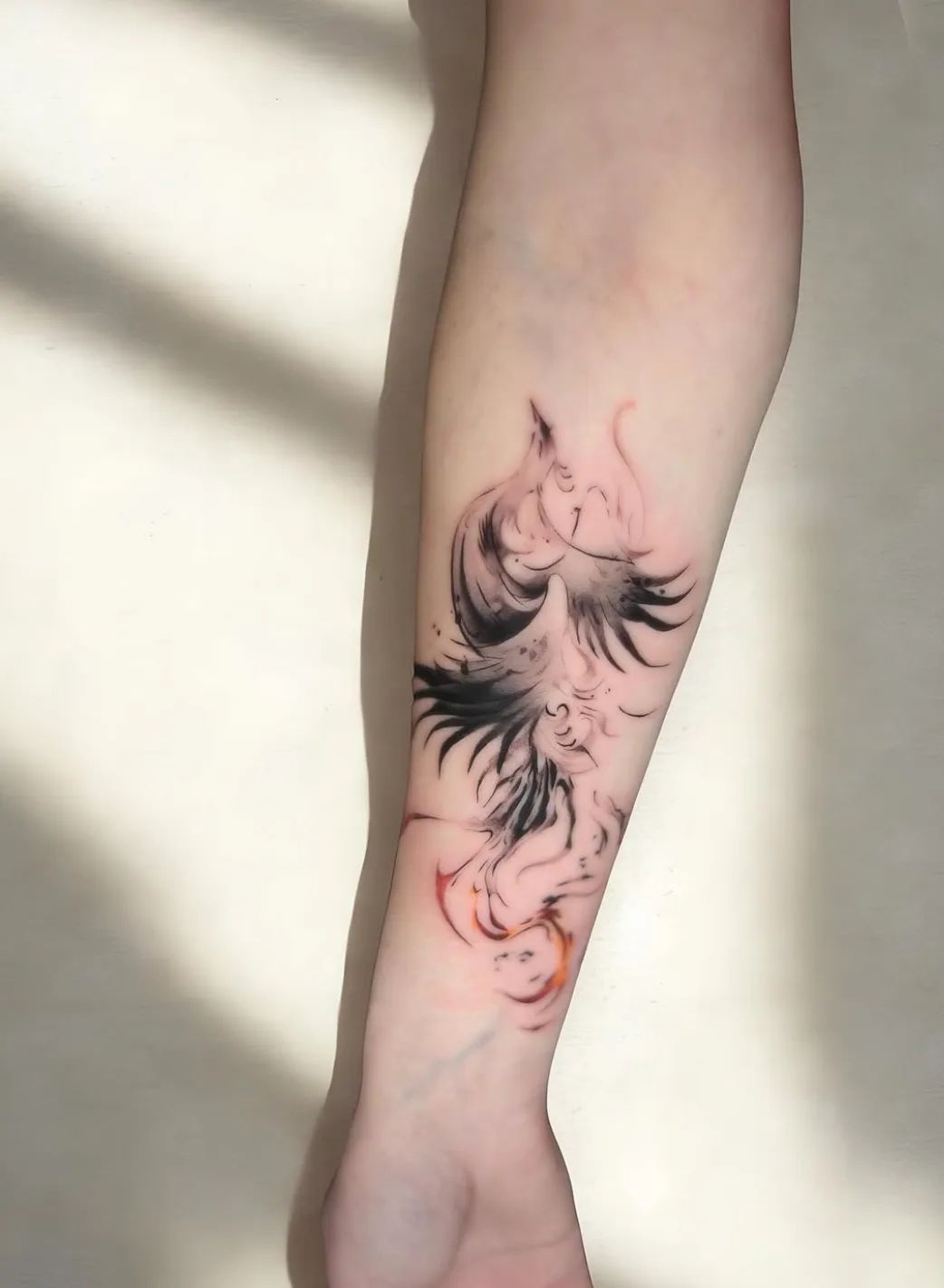 Abstract phoenix tattoo in black and red on forearm