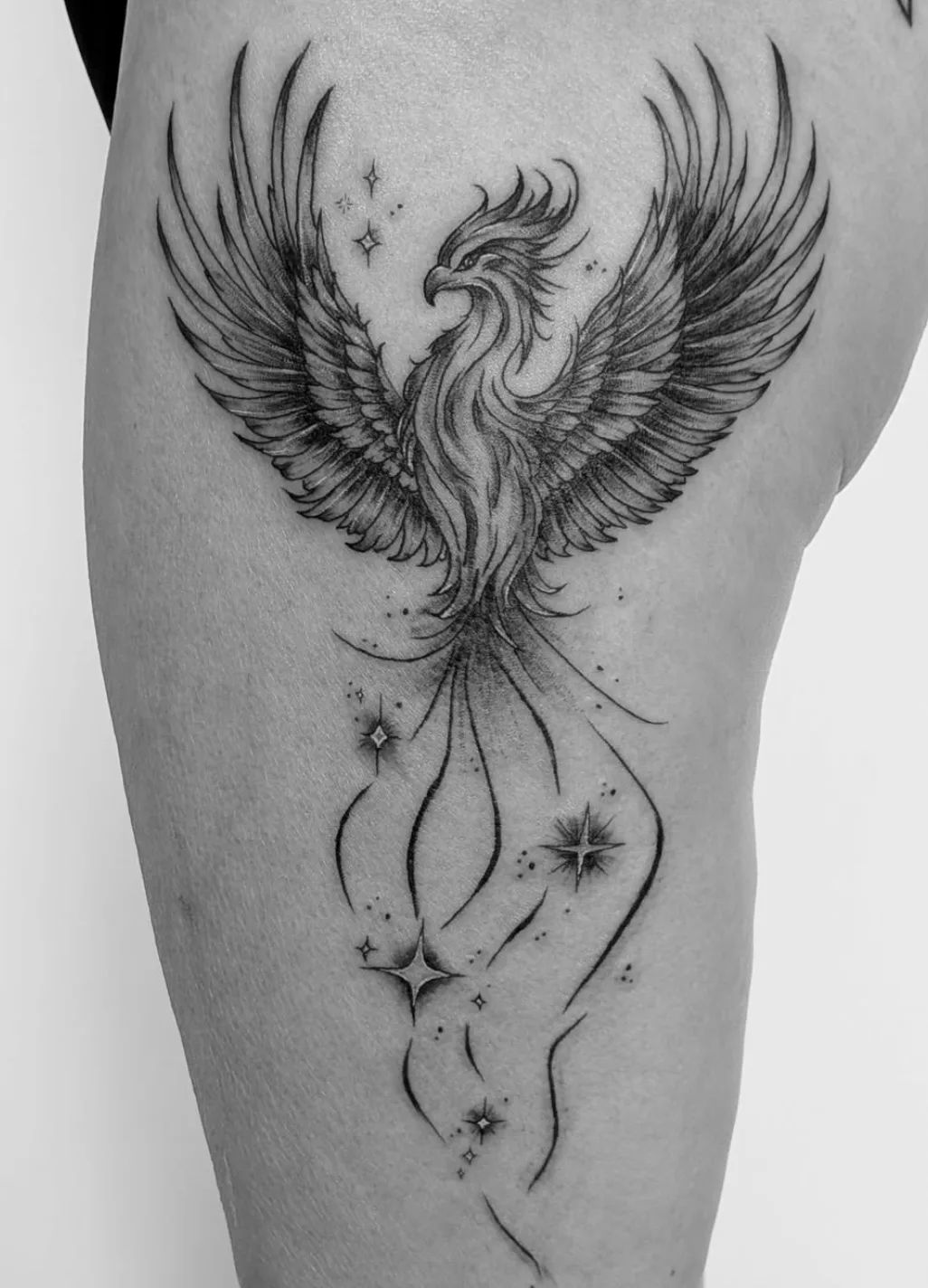 Fine line phoenix tattoo with stars on thigh