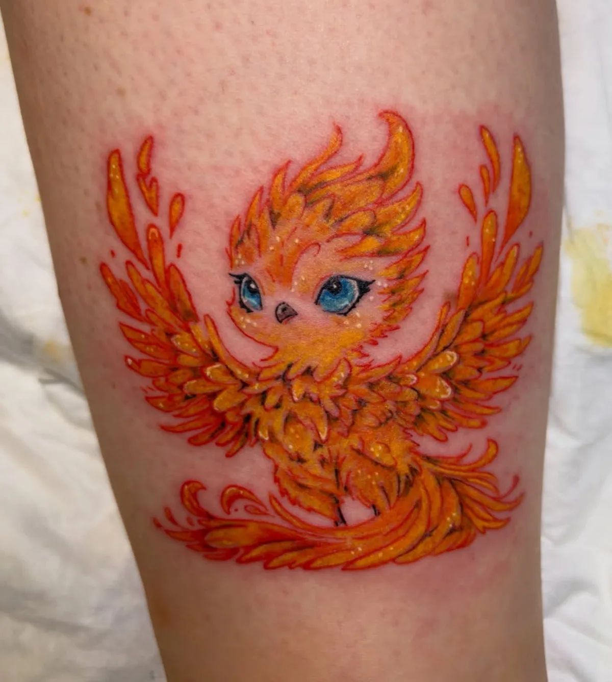 Colorful kawaii style phoenix tattoo with blue eyes on leg