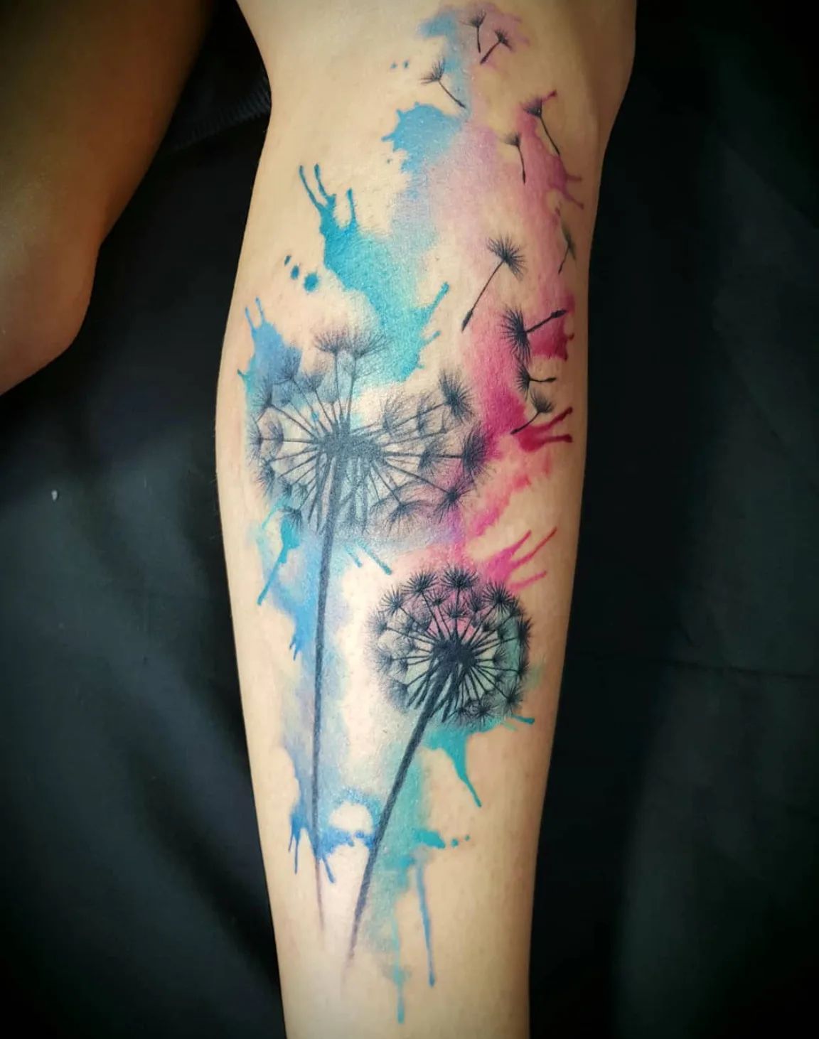 Dandelion tattoo in watercolor style with blue and pink paint splatters on the leg