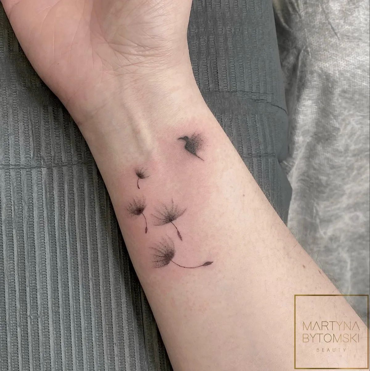 Fine line dandelion tattoo on forearm with flying seeds and bird