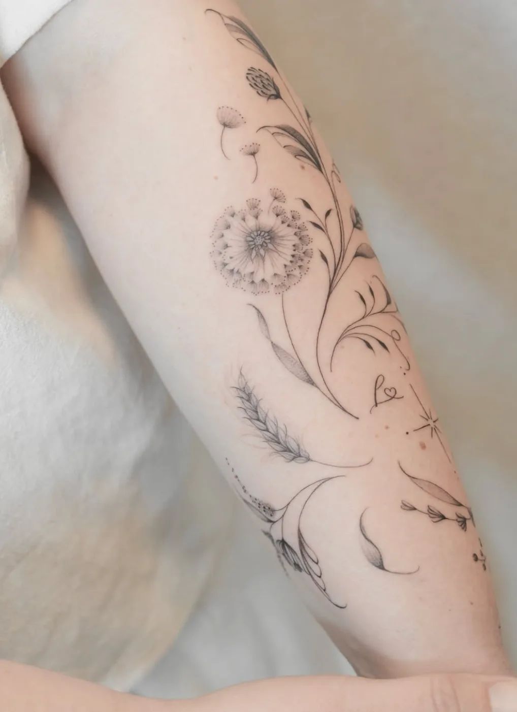 Dandelion tattoo in fineline style with wheat ear and leaves on forearm