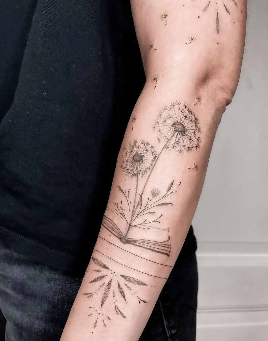 Dandelion fine line tattoo on forearm with book and flying seeds