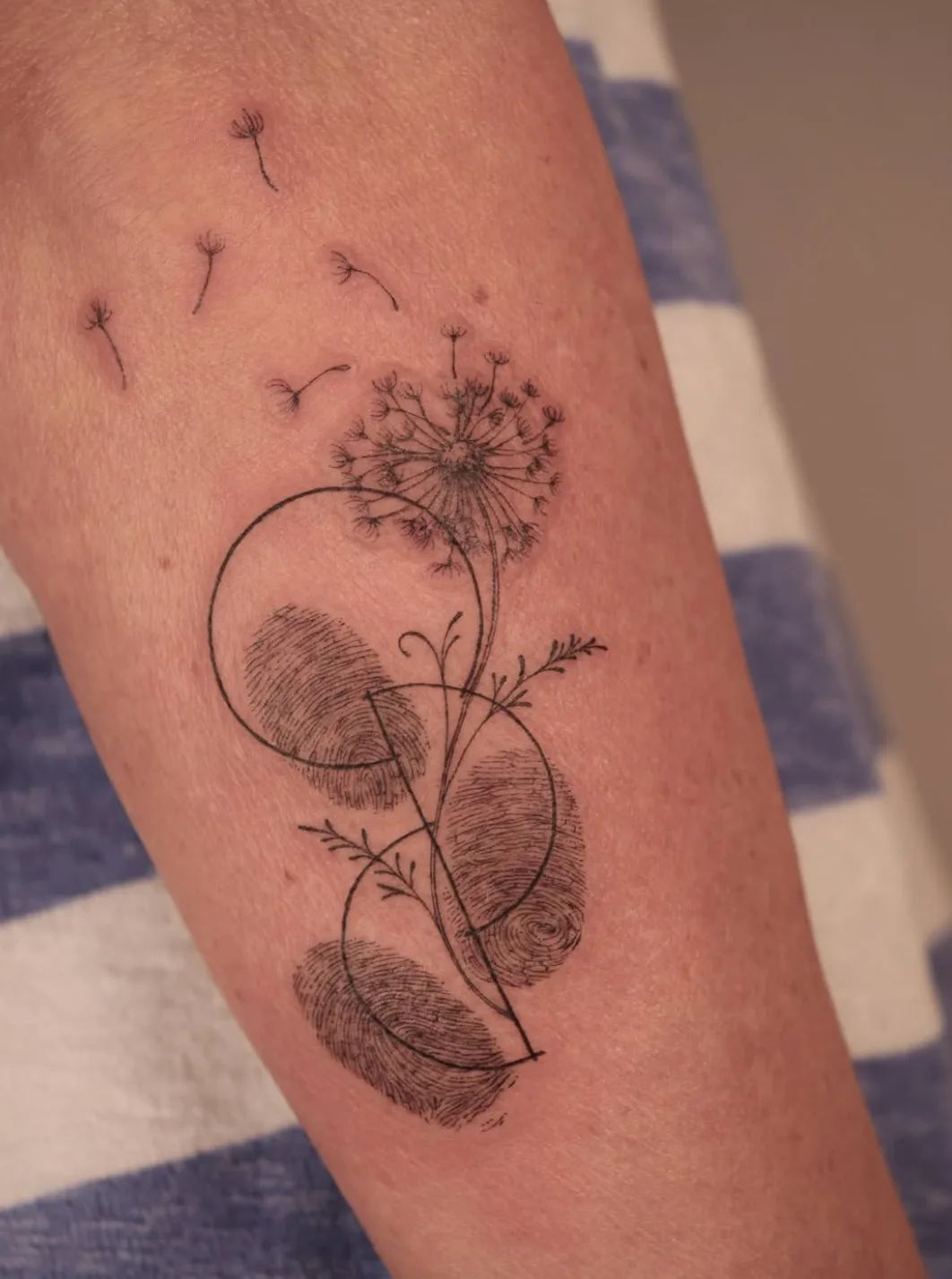 Dandelion tattoo with fingerprints and geometric circles in fine line style on forearm