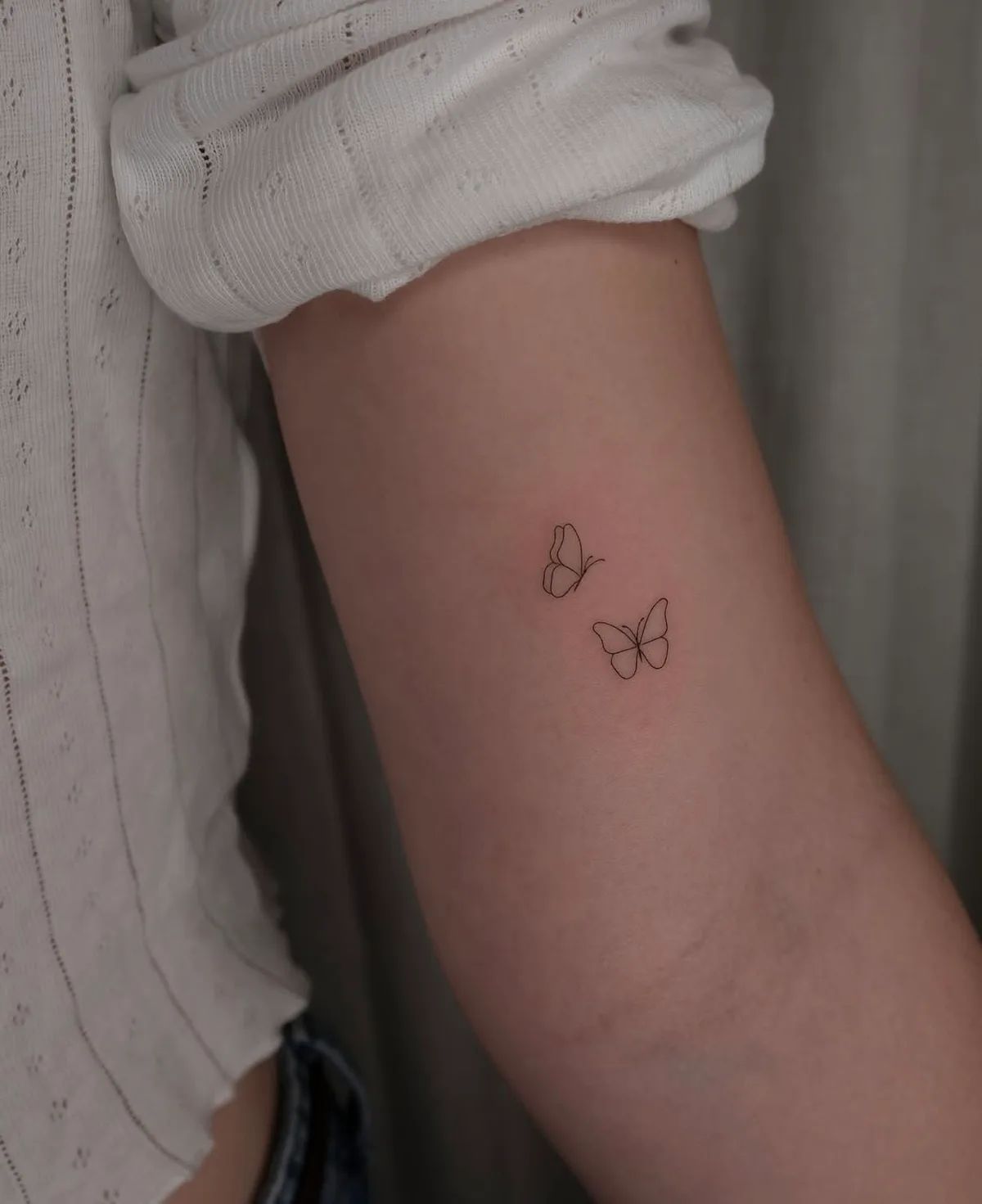 Zwei Schmetterling Fineline Tattoos am Oberarm