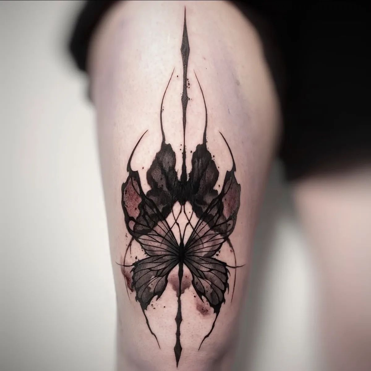 Schmetterling Tattoo im Blackwork-Stil mit roten Akzenten am Oberschenkel