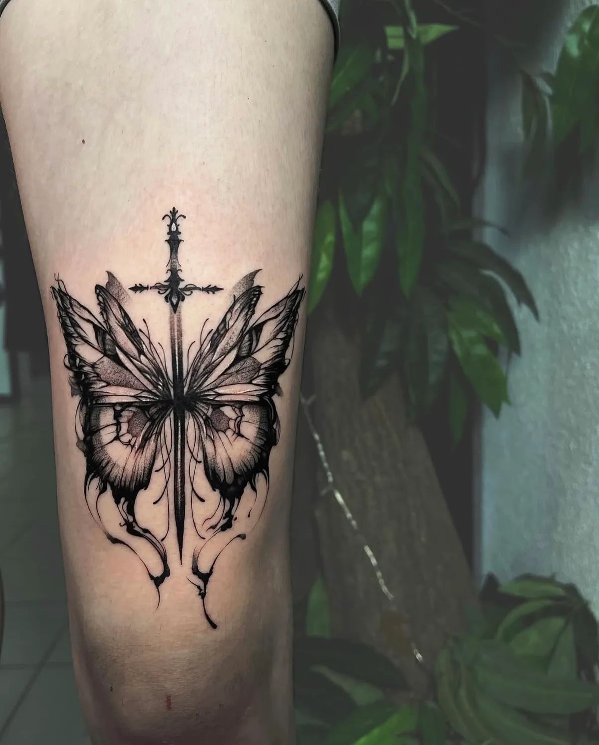 Schmetterling Tattoo mit Schwert im Fineline-Stil am Oberschenkel