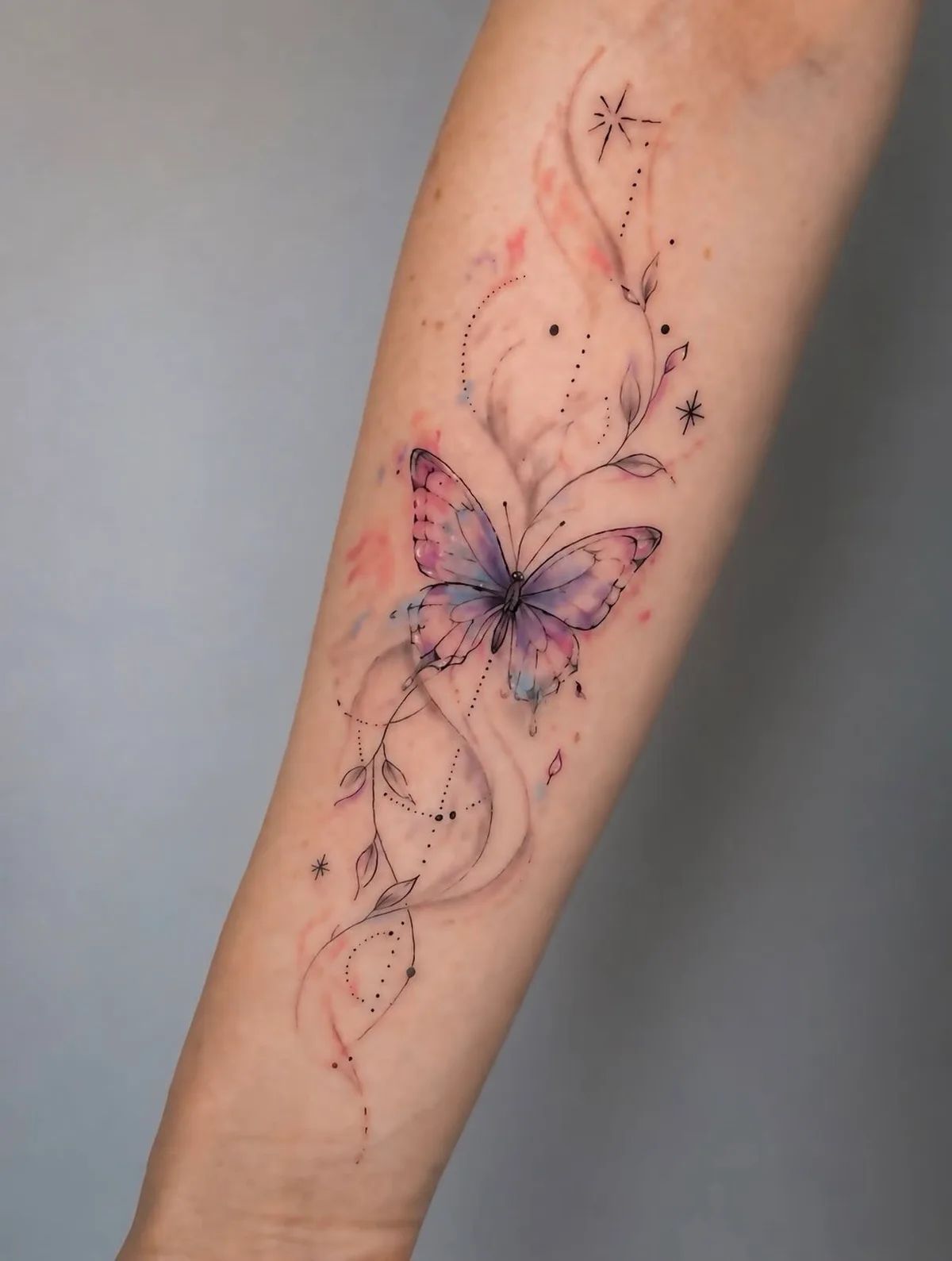 Schmetterling Tattoo in Aquarell und Fineline am Unterarm mit Ranken und Sternen