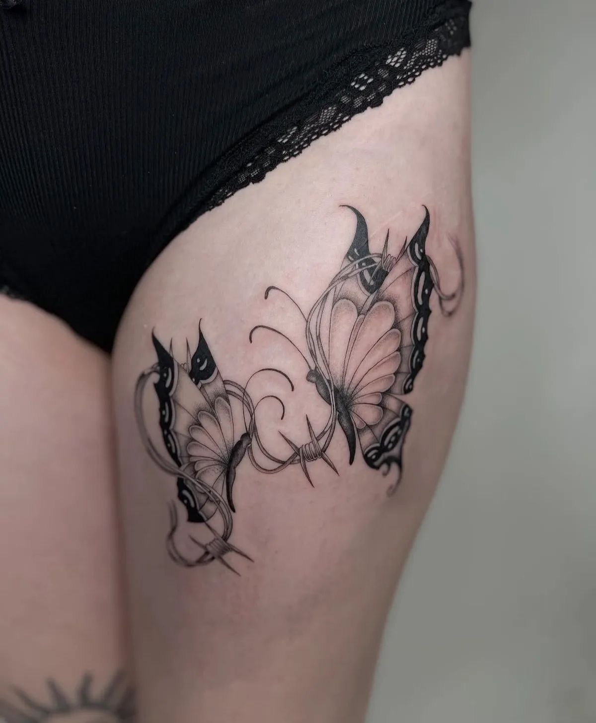 Schmetterling Tattoo im Blackwork Stil mit Stacheldraht am Oberschenkel