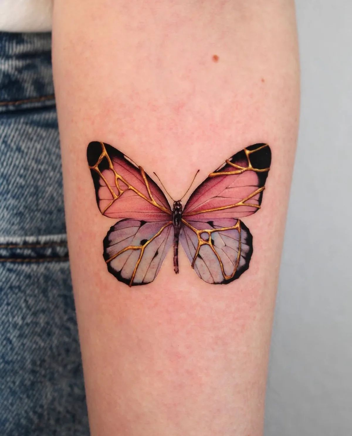 Schmetterling Tattoo in Pink und Lila mit goldenen Akzenten im Fineline-Stil am Unterarm