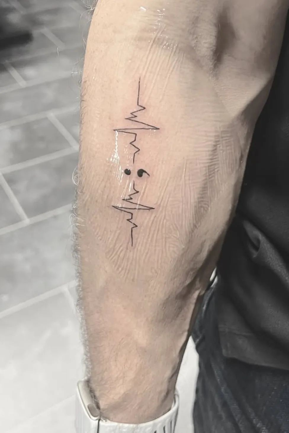 Semicolon tattoo with heartbeat line in fine line style on upper arm