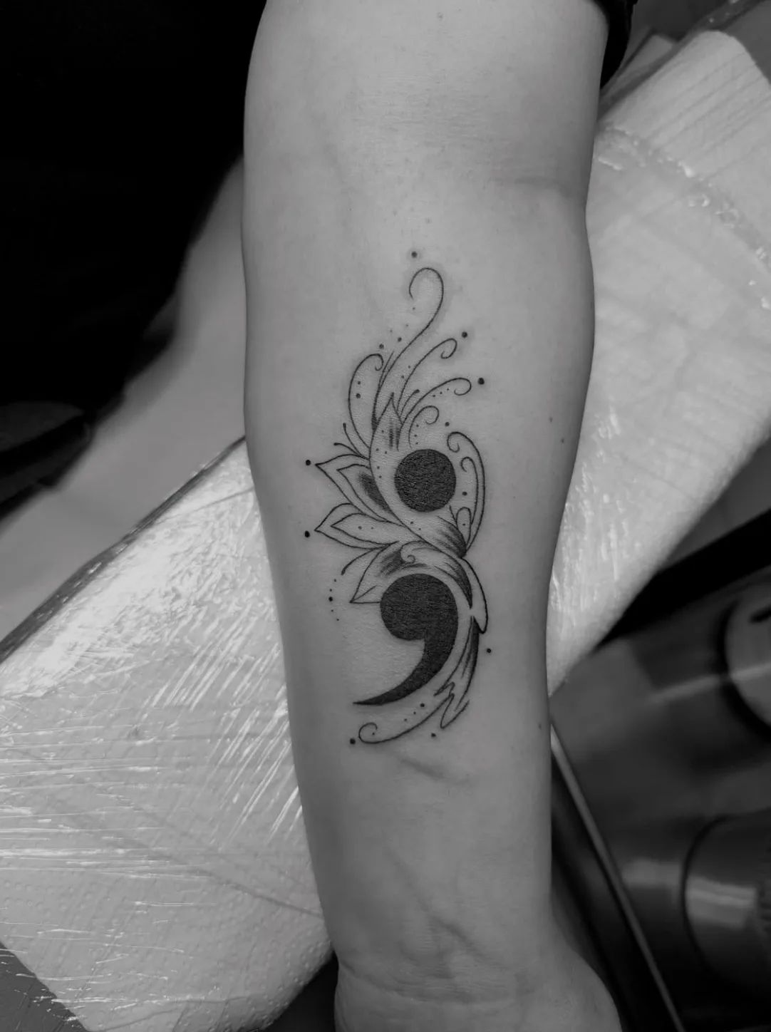 Semicolon tattoo with floral elements in fine line style on forearm