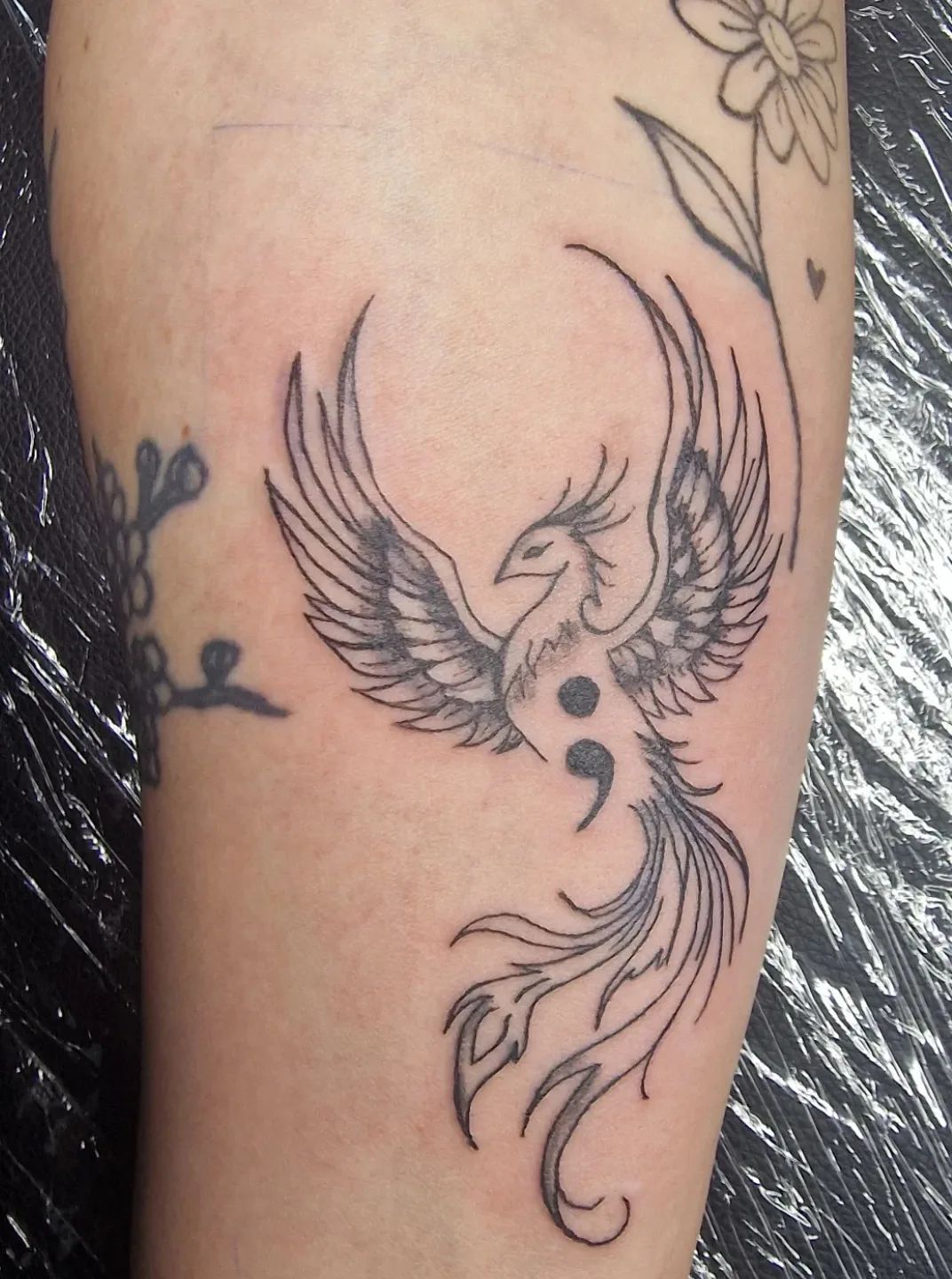 Phoenix tattoo with semicolon in fine line style on upper arm