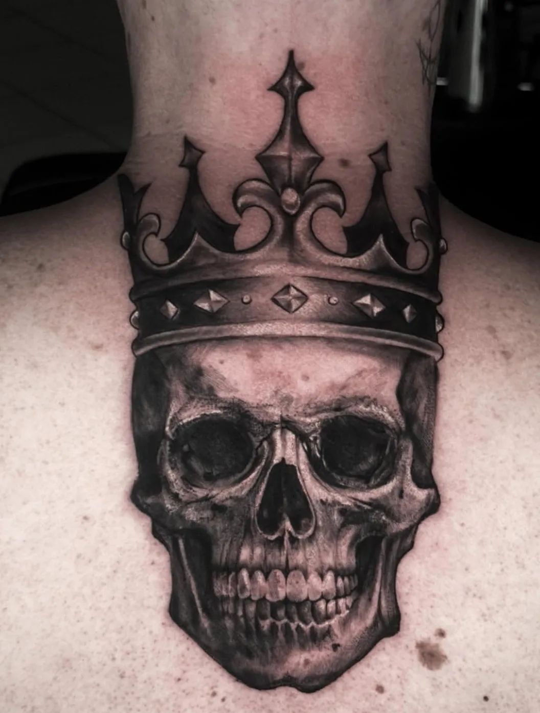 Skull tattoo with crown in black and grey style on the neck by daria