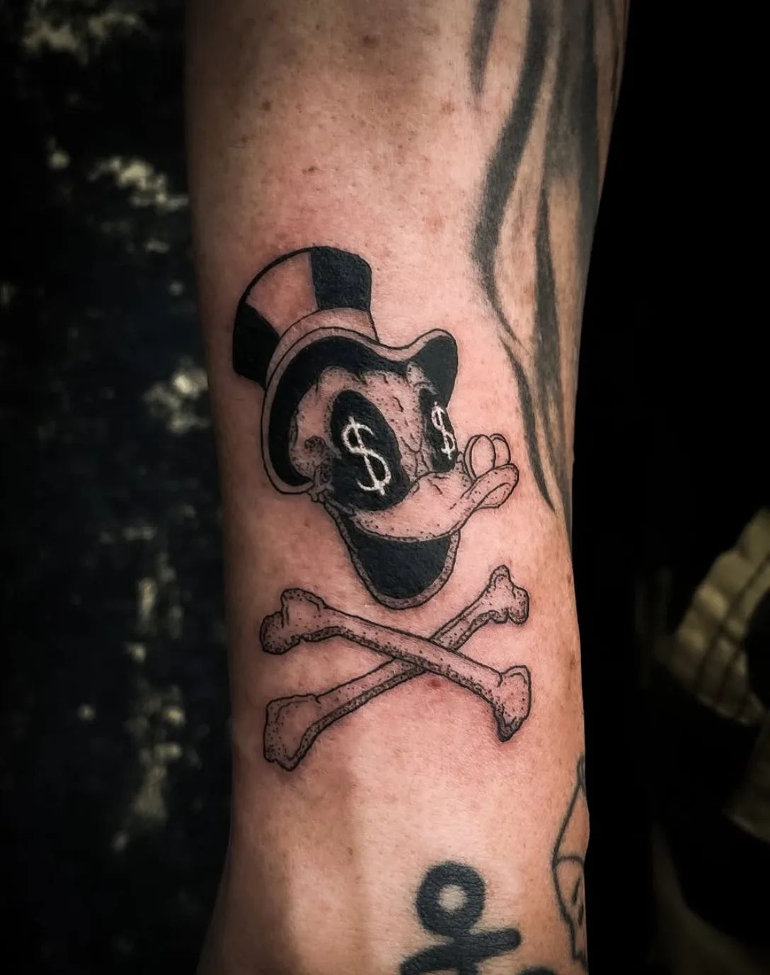 Skull duck with top hat and dollar signs in eyes, crossed bones, comic style on forearm