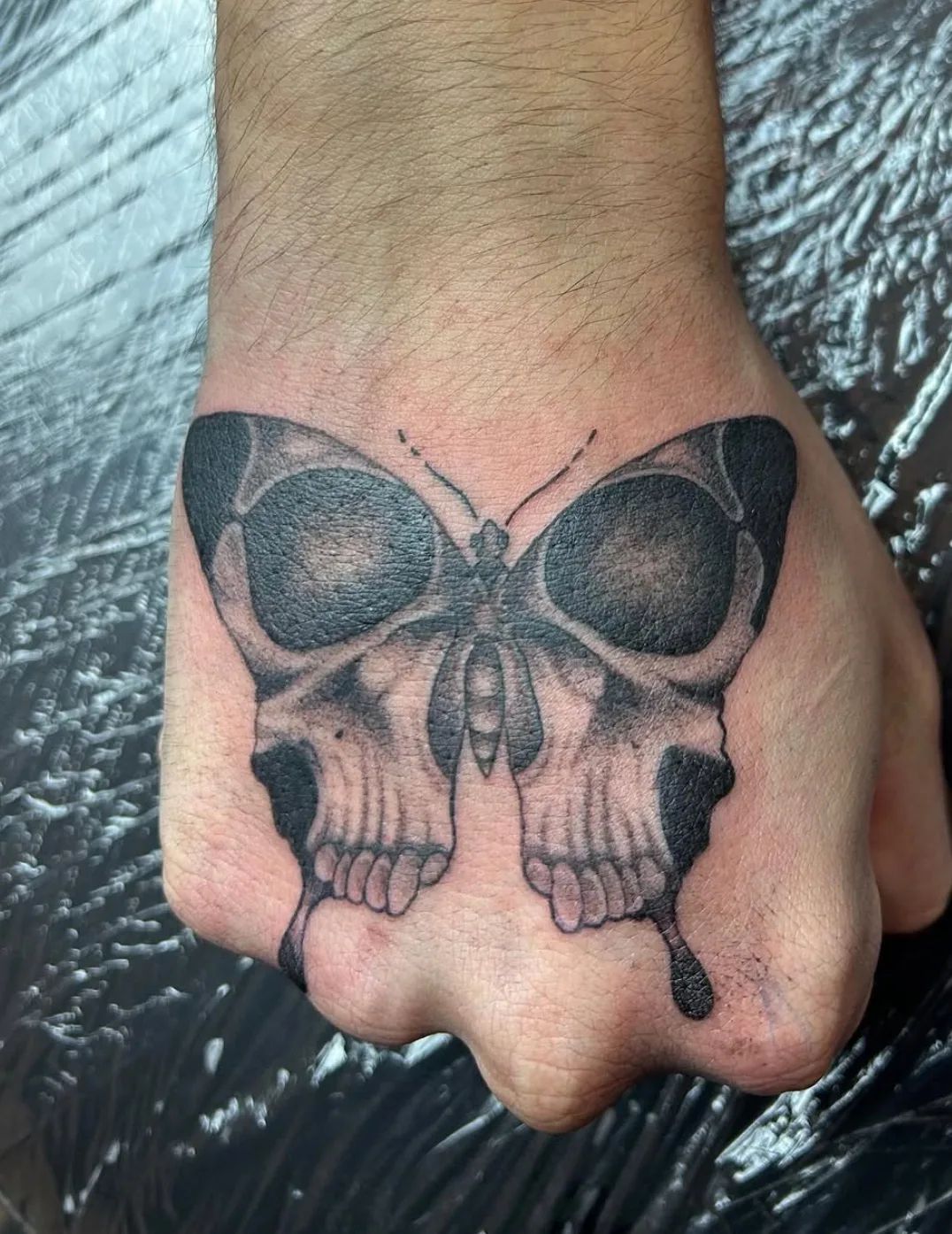 Skull butterfly tattoo in blackwork style on the back of the hand