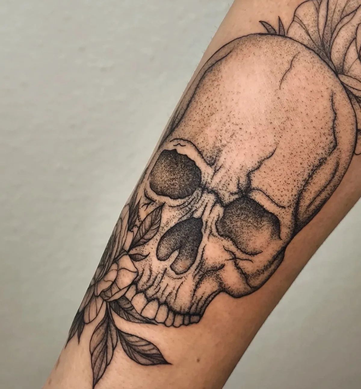 Dotwork skull tattoo with flowers and leaves on forearm
