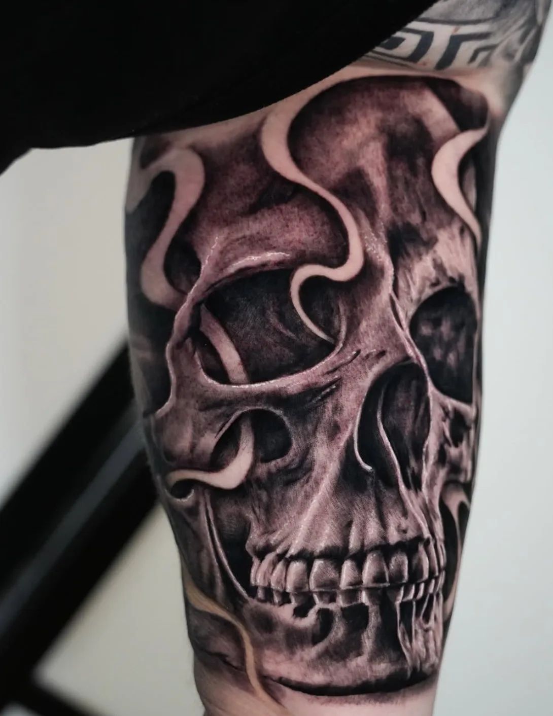 Realistic skull tattoo with smoke on the upper arm in black and grey