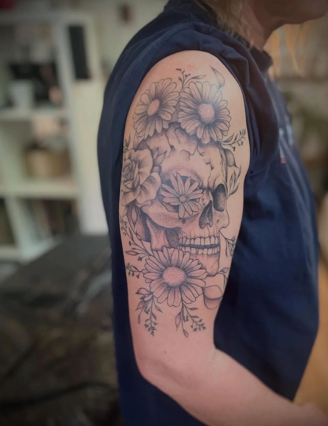 Skull tattoo with flowers and leaves in fineline style on upper arm