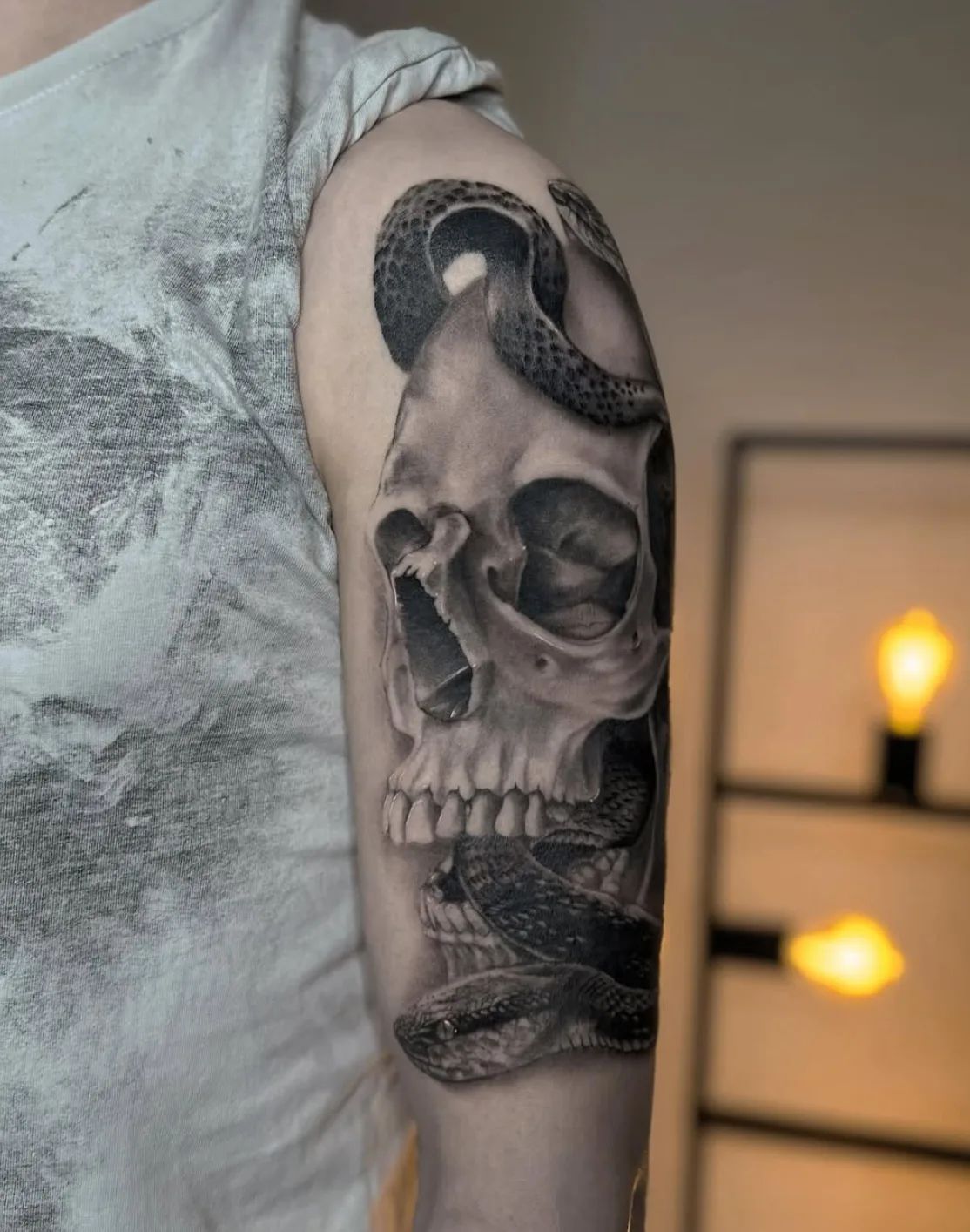 Realistic skull and snake tattoo on upper arm, black and grey