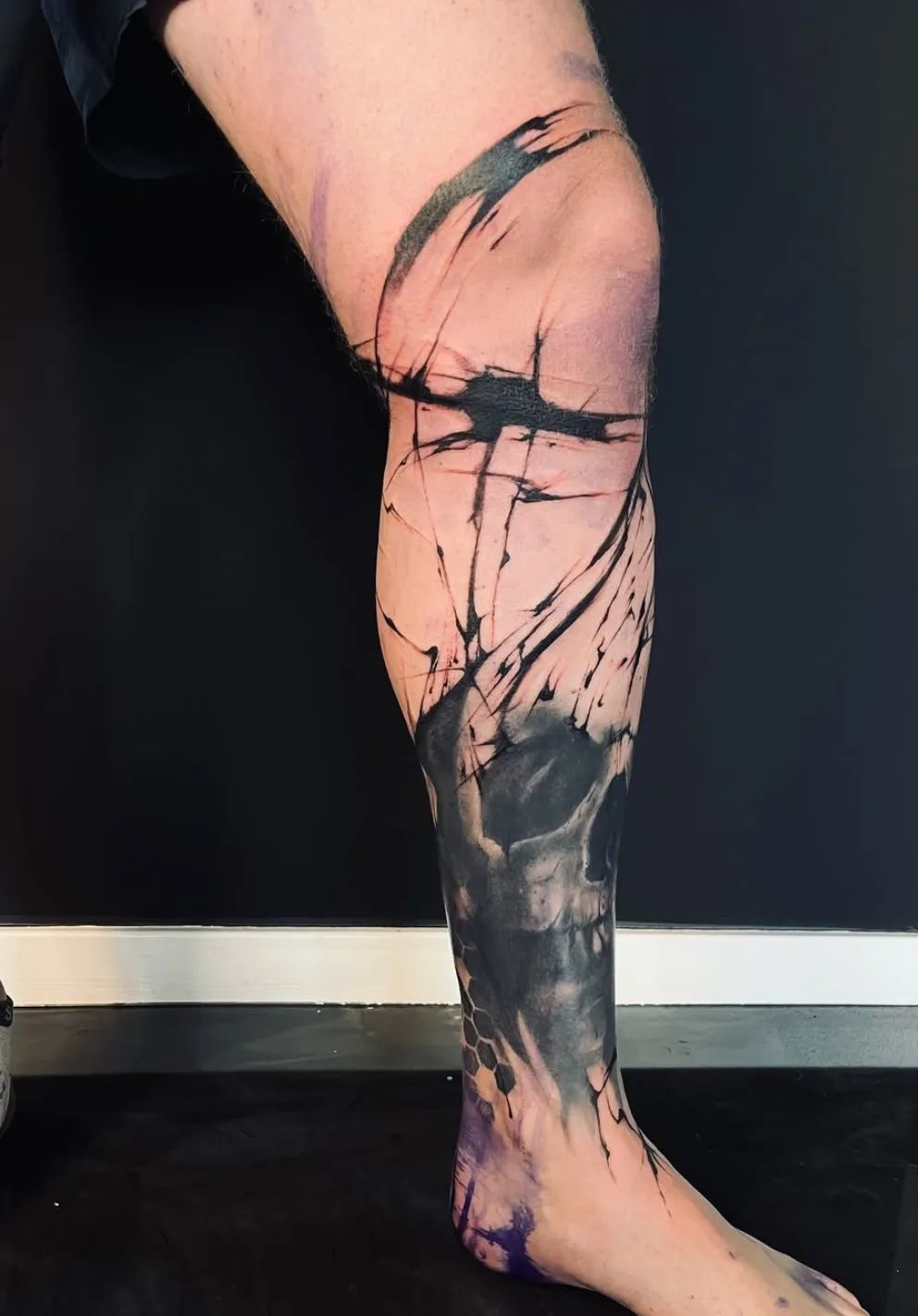 Skull tattoo in Trash Polka style on leg with abstract elements and paint splatters
