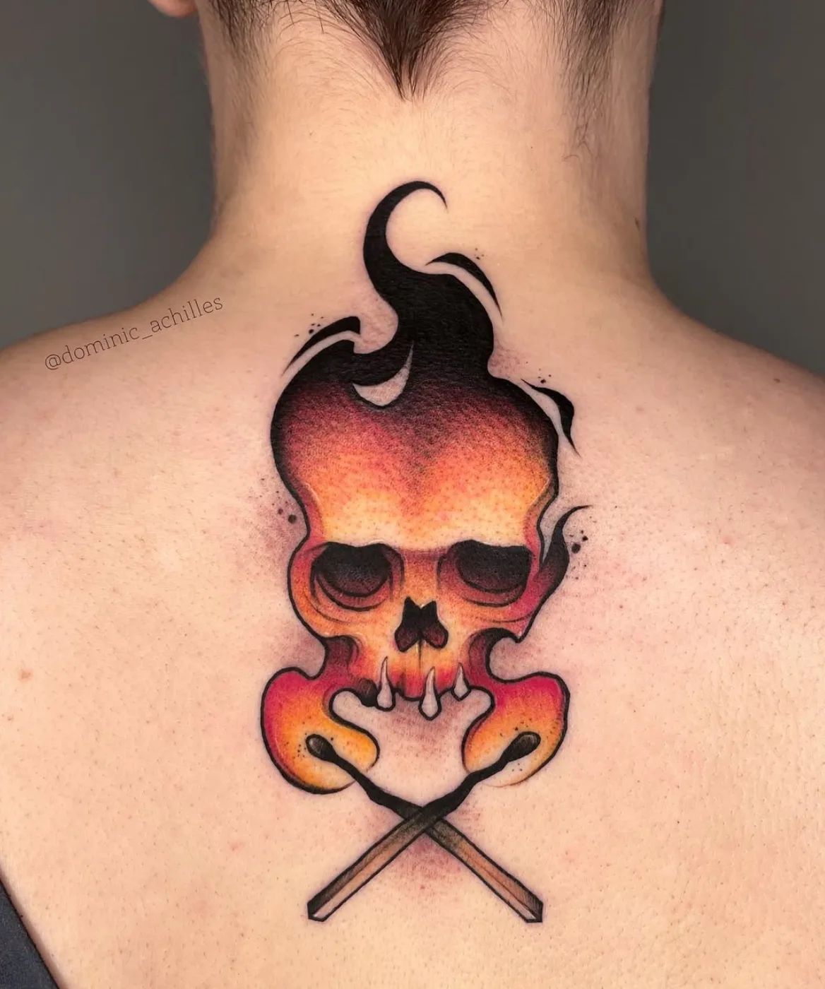 Flaming skull with crossed matches tattoo in New School style on upper back
